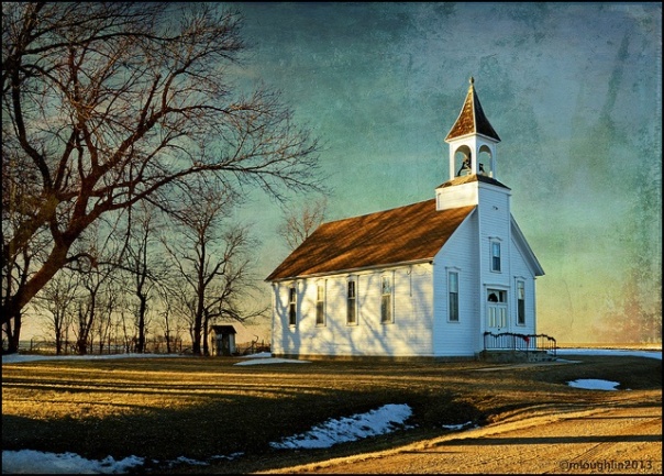 Small white wooden church at sunset.  Barren trees to the left, traces of snow on the ground, 